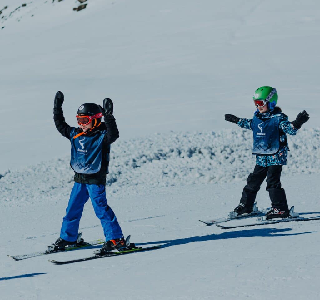 Kinderen skiën de berg af met hun handen in de lucht